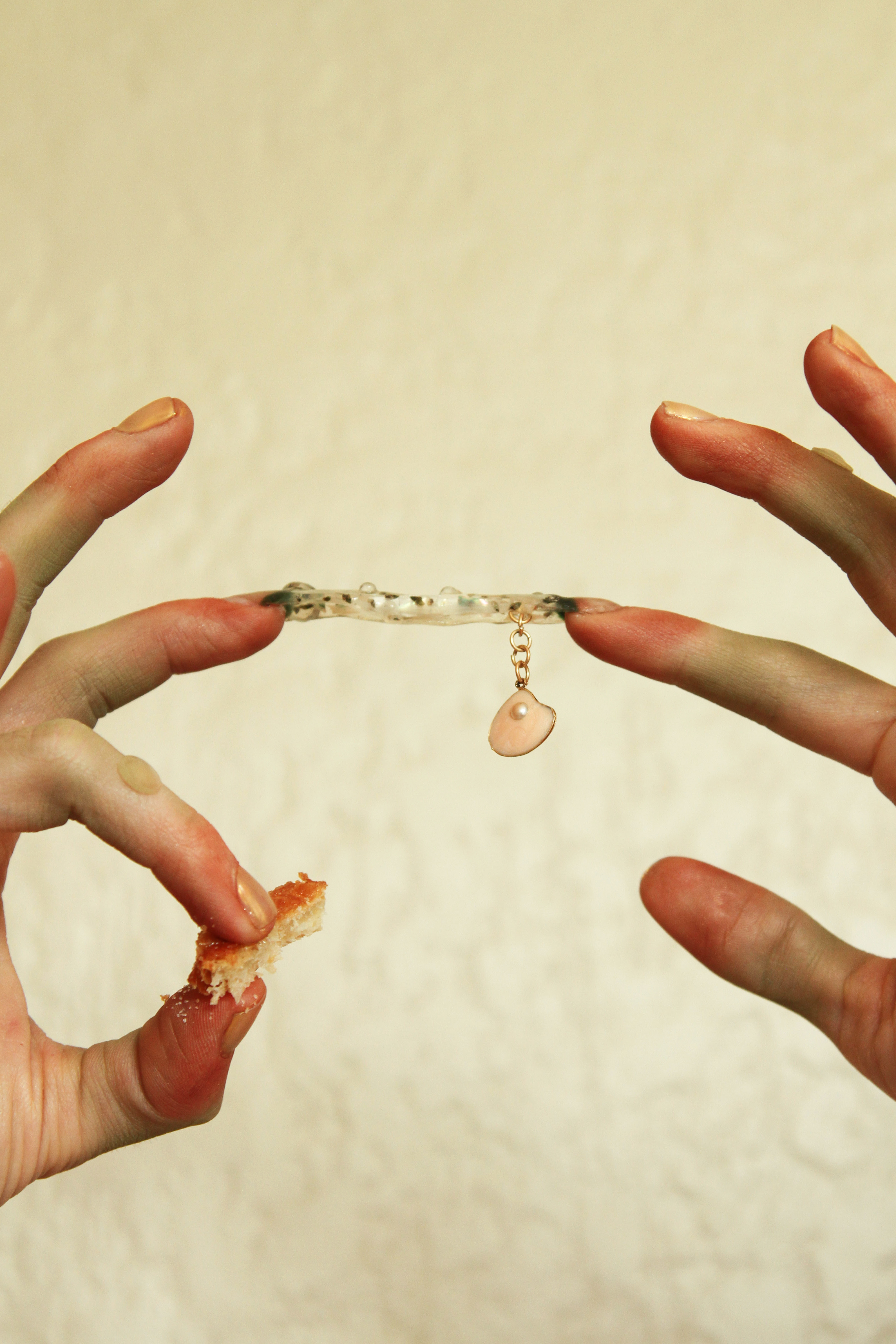 Two pointer fingers connected by a transparent nail sculpture full of tiny snails with the left hand carrying a biscuit